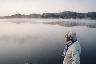 Senior man looking at view while standing against lake