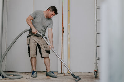 A young man vacuums the floor with a construction vacuum cleaner.