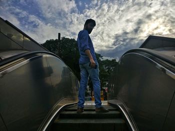 Rear view of man standing on car against sky