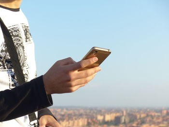 Close-up of man using mobile phone against clear sky