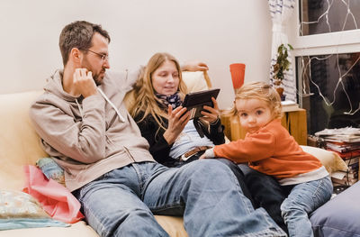 Mother and father using digital tablet by daughter playing on sofa at home