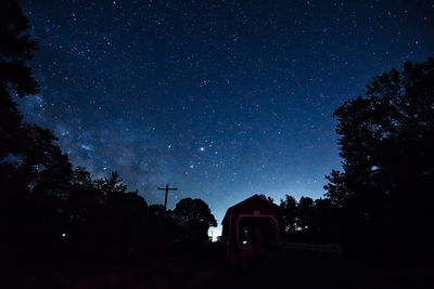 Covered bridge amidst silhouette trees against sky at night