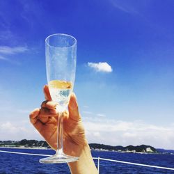 Cropped image of person holding champagne by sea against sky