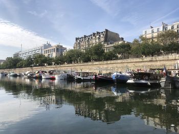 Sailboats moored on lake by buildings in city against sky