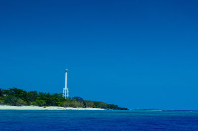 Lighthouse by sea against blue sky