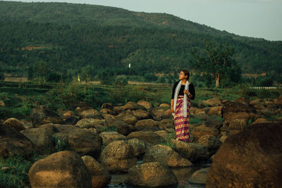 Full length of young woman standing on rock against sky