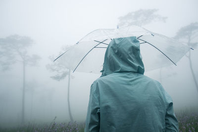 Rear view of woman holding umbrella while standing outdoors during rainfall