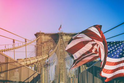 Low angle view of american flag against brooklyn bridge during sunset
