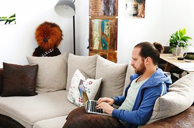 Bearded mid adult man using laptop while sitting on sofa at home
