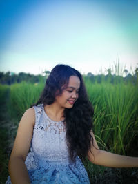 Beautiful young woman looking away on field against sky