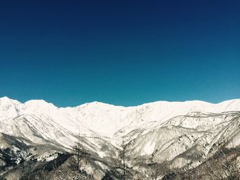 Scenic view of snow covered mountains against clear blue sky