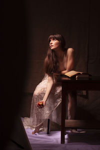 Shirtless young woman holding apple while sitting on table 