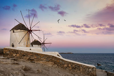 View of traditional windmill by sea against sky during sunset