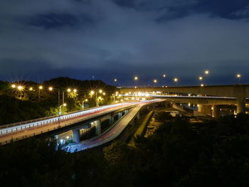 Light trails on bridge in city against sky at night