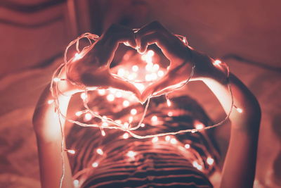 High angle view of hands forming heart shape next to illuminated lights