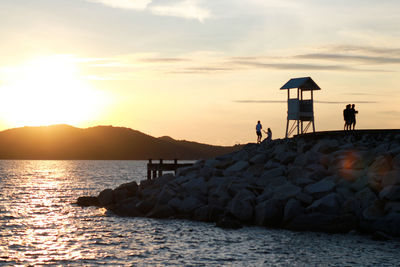 People on rock by sea against sky during sunset