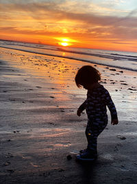 Boy standing on beach against sky during sunset