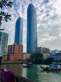 Modern buildings by river against sky in city