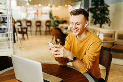 Young woman using mobile phone while sitting on table