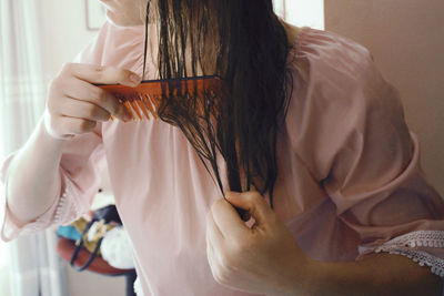 Midsection of woman combing hair at home