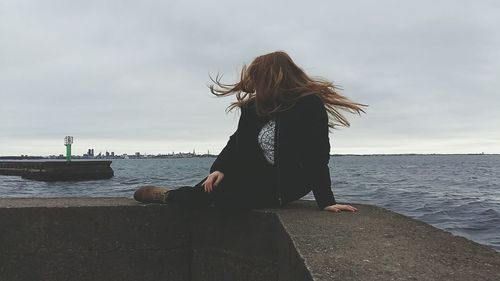 Woman sitting on retaining wall against sea