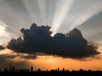 Low angle view of sunlight streaming through silhouette during sunset