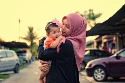 Mother carrying daughter while standing on road