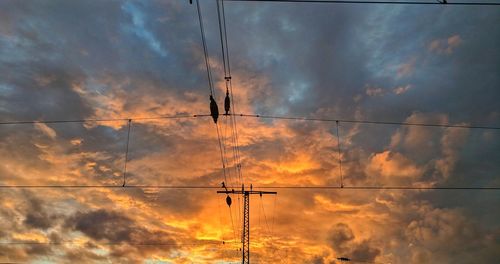 Low angle view of silhouette electricity pylon against dramatic sky