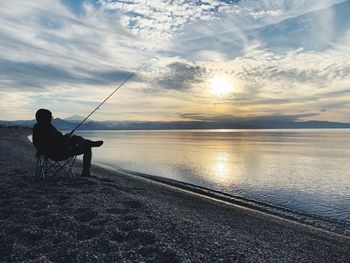 Man fishing in sea against sky during sunset