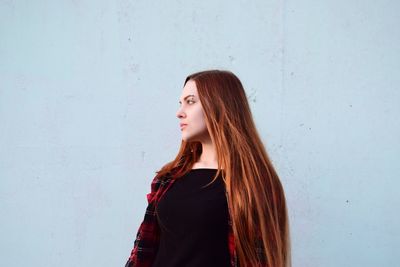 Thoughtful young woman looking away while standing against wall