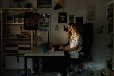 Teenage girls using computer at table in darkroom at home