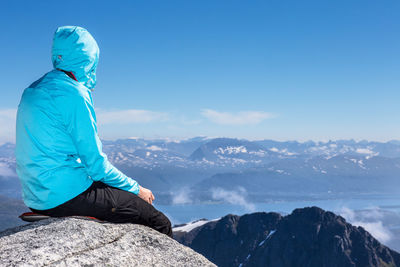 Person sitting on rock against mountains and blue sky