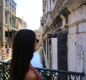 Rear view of woman photographing buildings in city