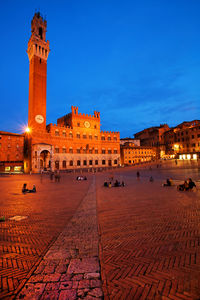 People relaxing by historic buildings at piazza del campo against sky during dusk