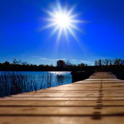 Wooden pier on calm lake against blue sky on sunny day