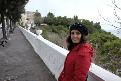 Portrait of smiling young woman standing by retaining wall