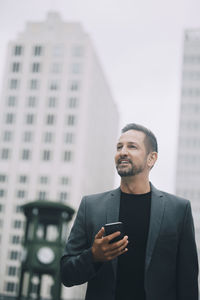 Confident mature businessman looking away while standing in city