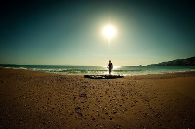 Woman standing on sea shore at beach against sky during sunny day