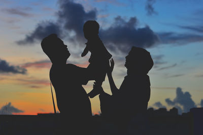 Silhouette friends with arms raised against sky during sunset