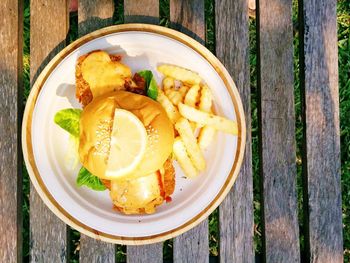 Directly above shot of fish burger with french fries served in plate on table