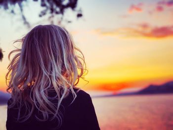 Rear view of woman standing by sea against sky during sunset