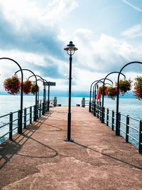 Street lights on footpath by sea against sky