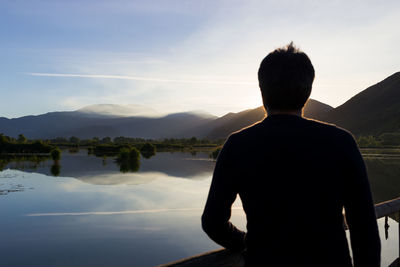 Rear view of man standing by lake against sky