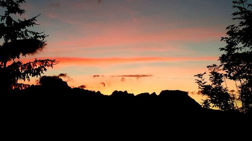 Silhouette trees against dramatic sky during sunset