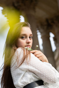 Portrait of young woman holding flowers standing outdoors