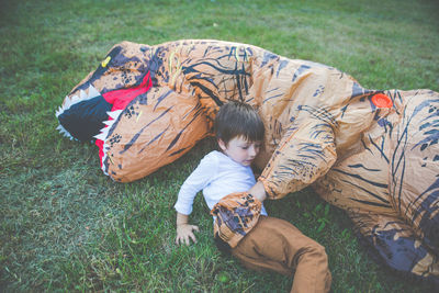 High angle view of boy lying with person wearing dinosaur costume in park