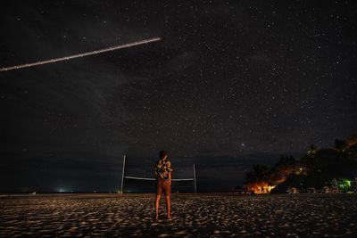 Rear view of woman standing on field against sky at night