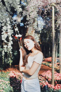 Young woman with eyes closed standing against plants in park