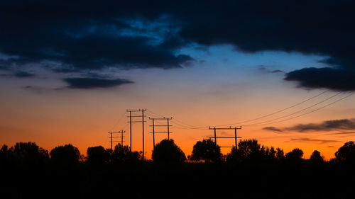 Silhouette trees and electricity pylon against romantic sky at sunset