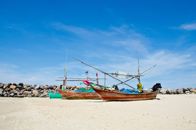 Boat moored on beach against blue sky